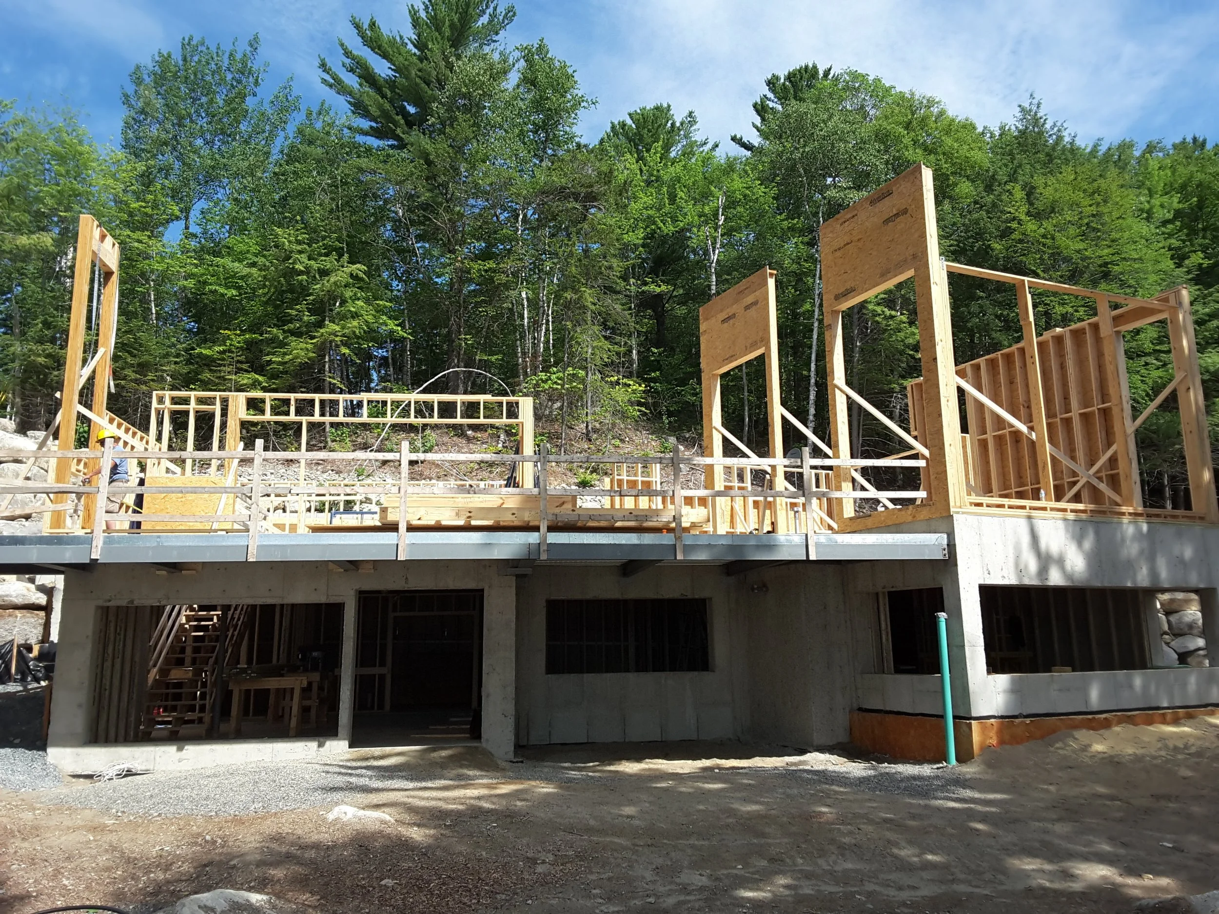 Wood framing construction of a building's lower level against a background of trees and a blue sky.