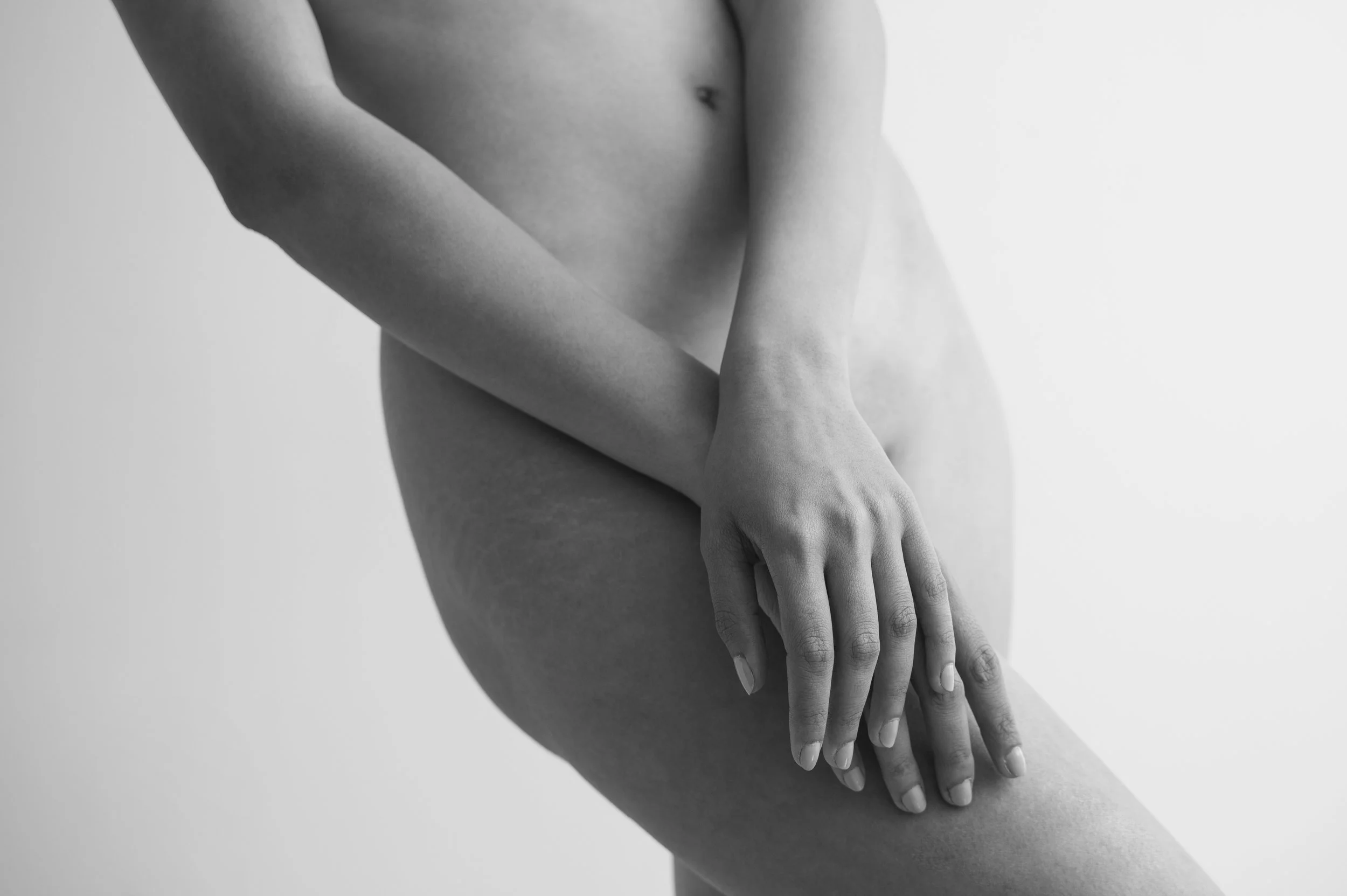Black and white photo of a nude person with their left hand resting on their right thigh.