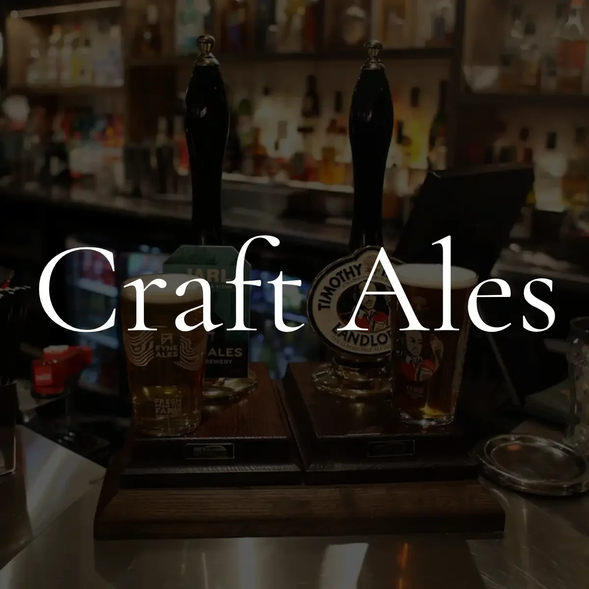 Two draft beer taps above glasses of beer on a bar counter, with a blurred background of bottles and bar shelves, and the text 'Craft Ales' overlaid.