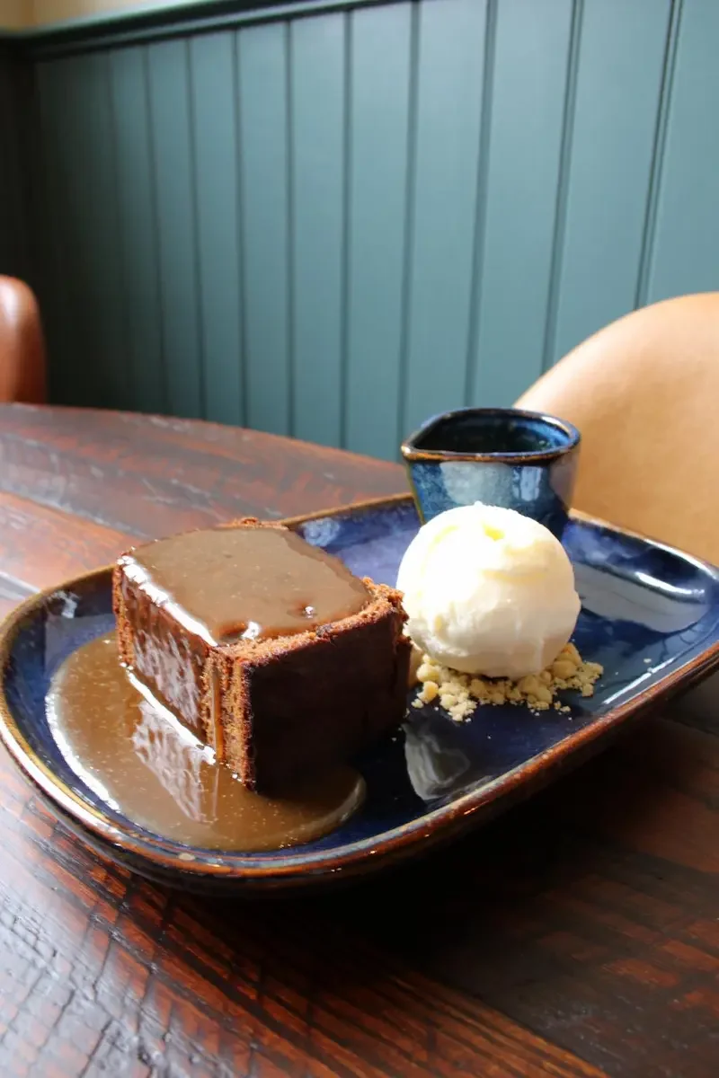 Chocolate lava cake with caramel sauce, a scoop of vanilla ice cream, and a small container of extra caramel sauce on a dark blue plate.