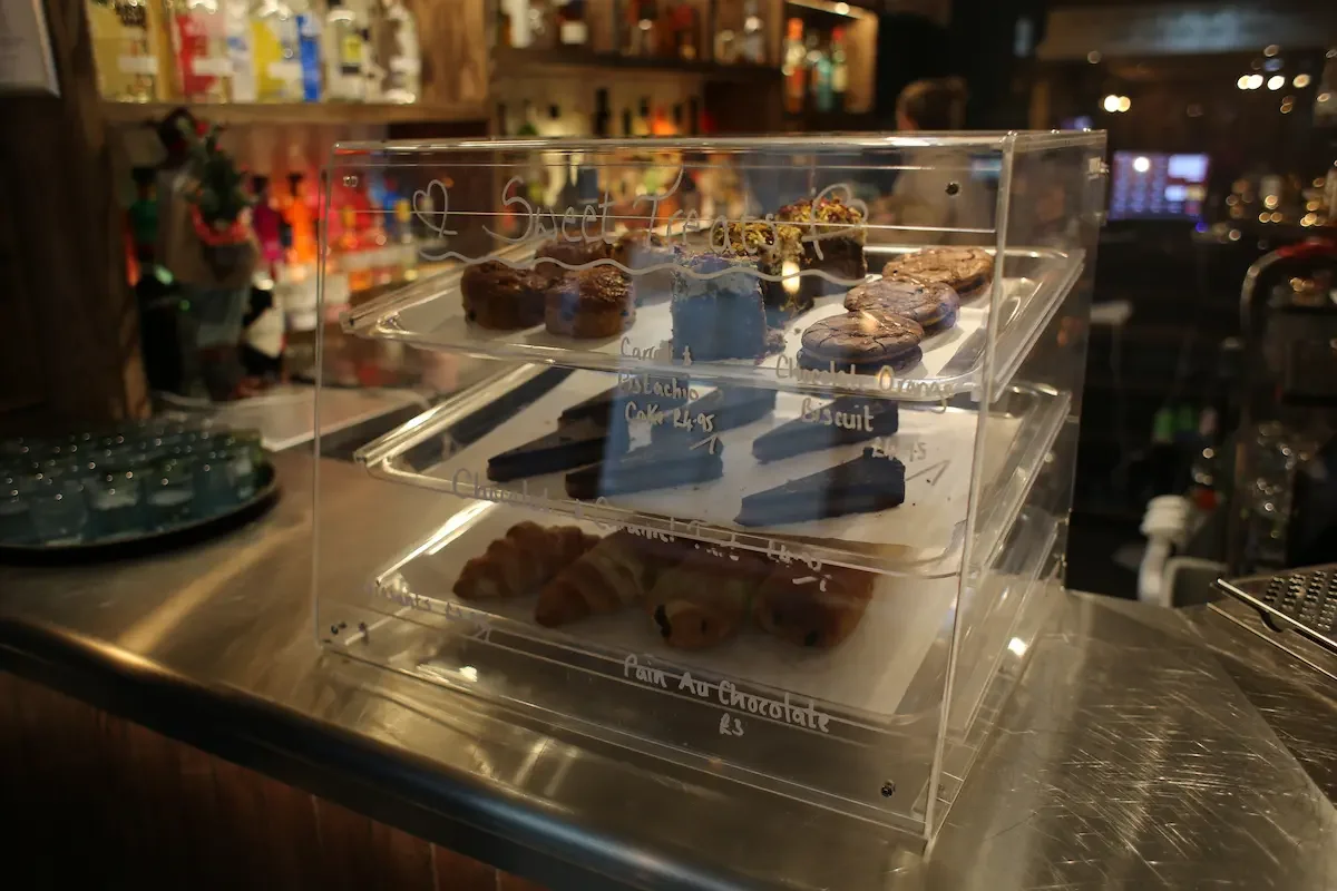 Display case with assorted baked goods including cookies, brownies, and croissants in a cafe or bakery setting.