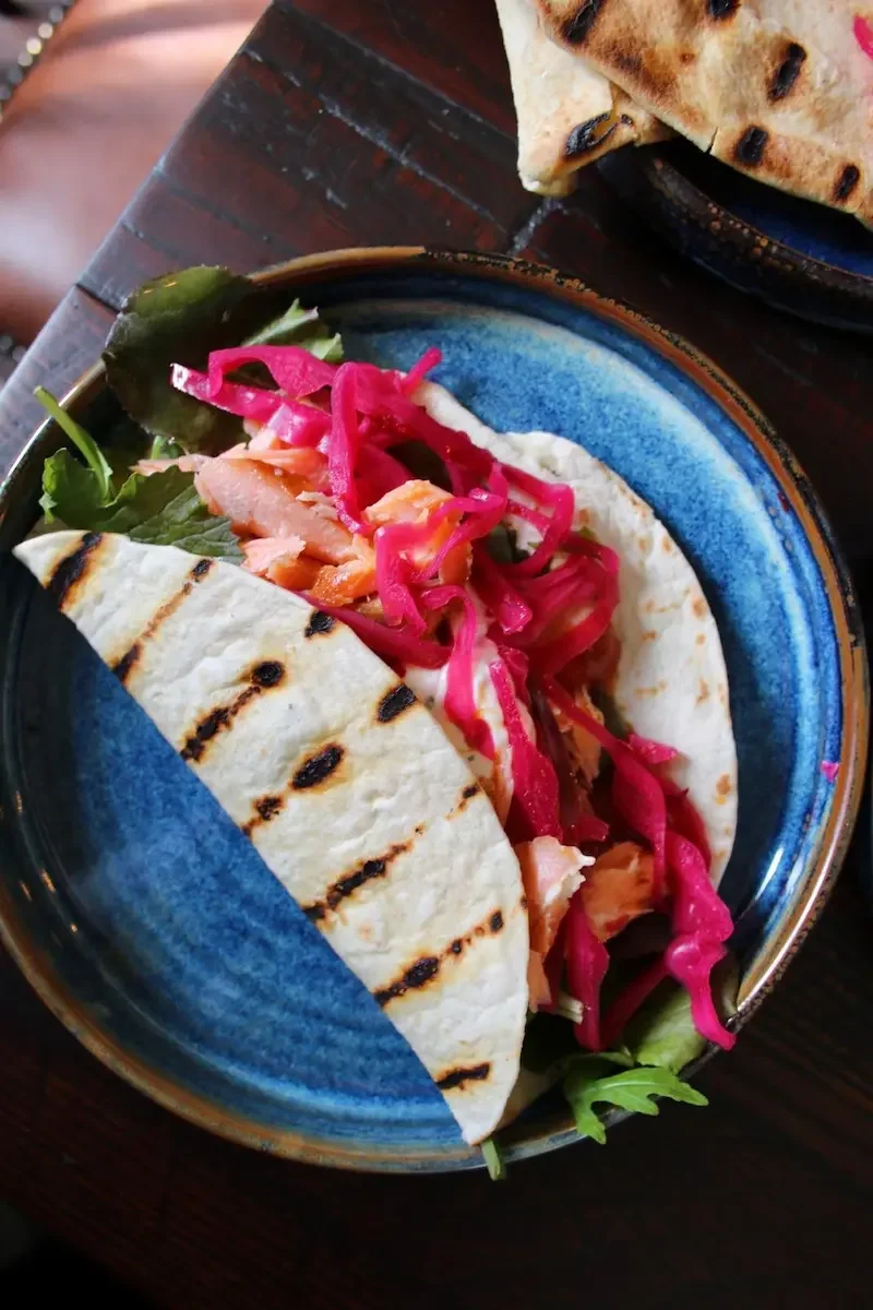 Grilled chicken soft taco with shredded lettuce, pickled red onions, and a side of naan bread on a blue ceramic plate.