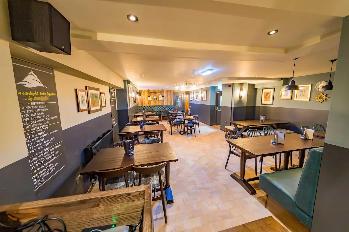Empty restaurant with wooden tables and black and green chairs, framed artwork on the walls, and warm lighting.
