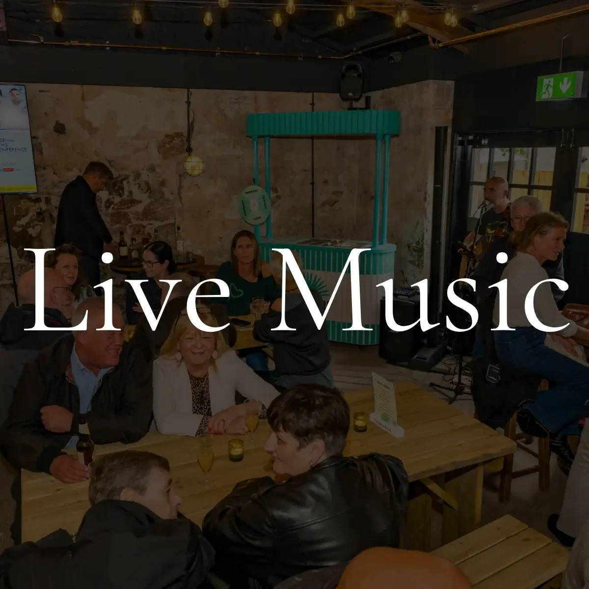 People enjoying live music at a restaurant or bar with exposed brick wall and bar counter in the background, and a sign that says "Live Music" overlaid on the image.