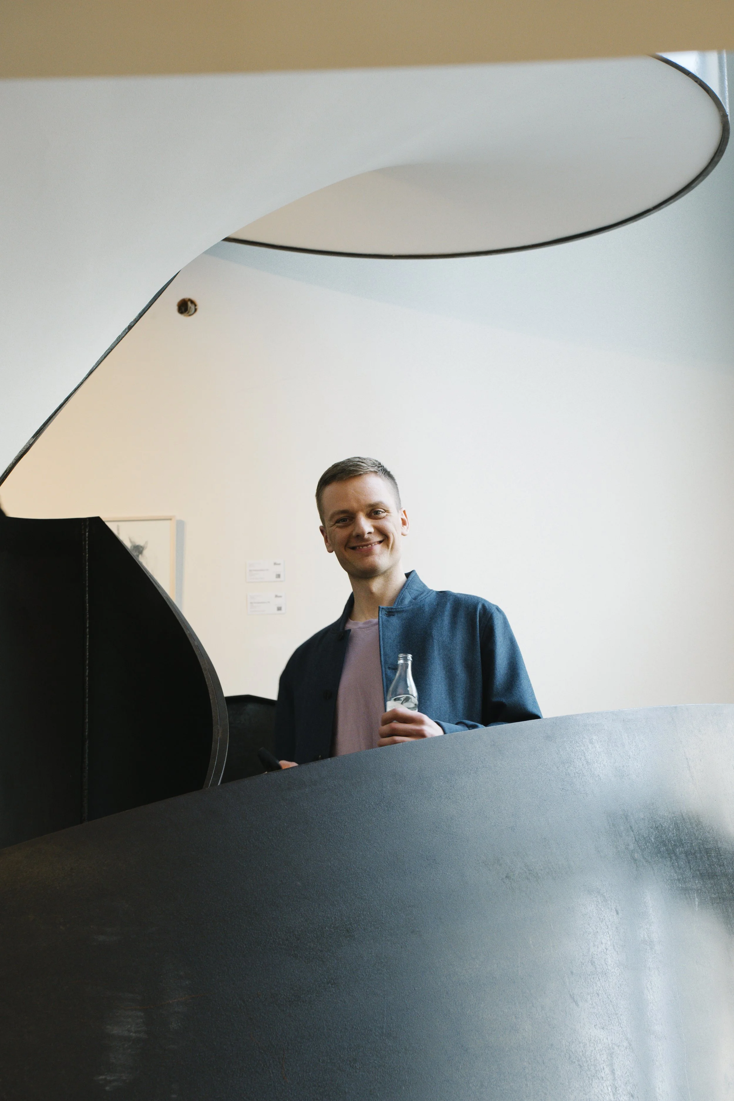 Junge Mann mit Getränk in der Hand steht an einem schwarzen Klavier in einem Kunstmuseum.