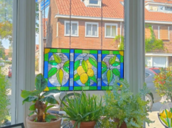 Kleurrijke stained glas raam met citroen en bladeren motieven, gezien vanaf een interieur met planten op een vensterbank.
