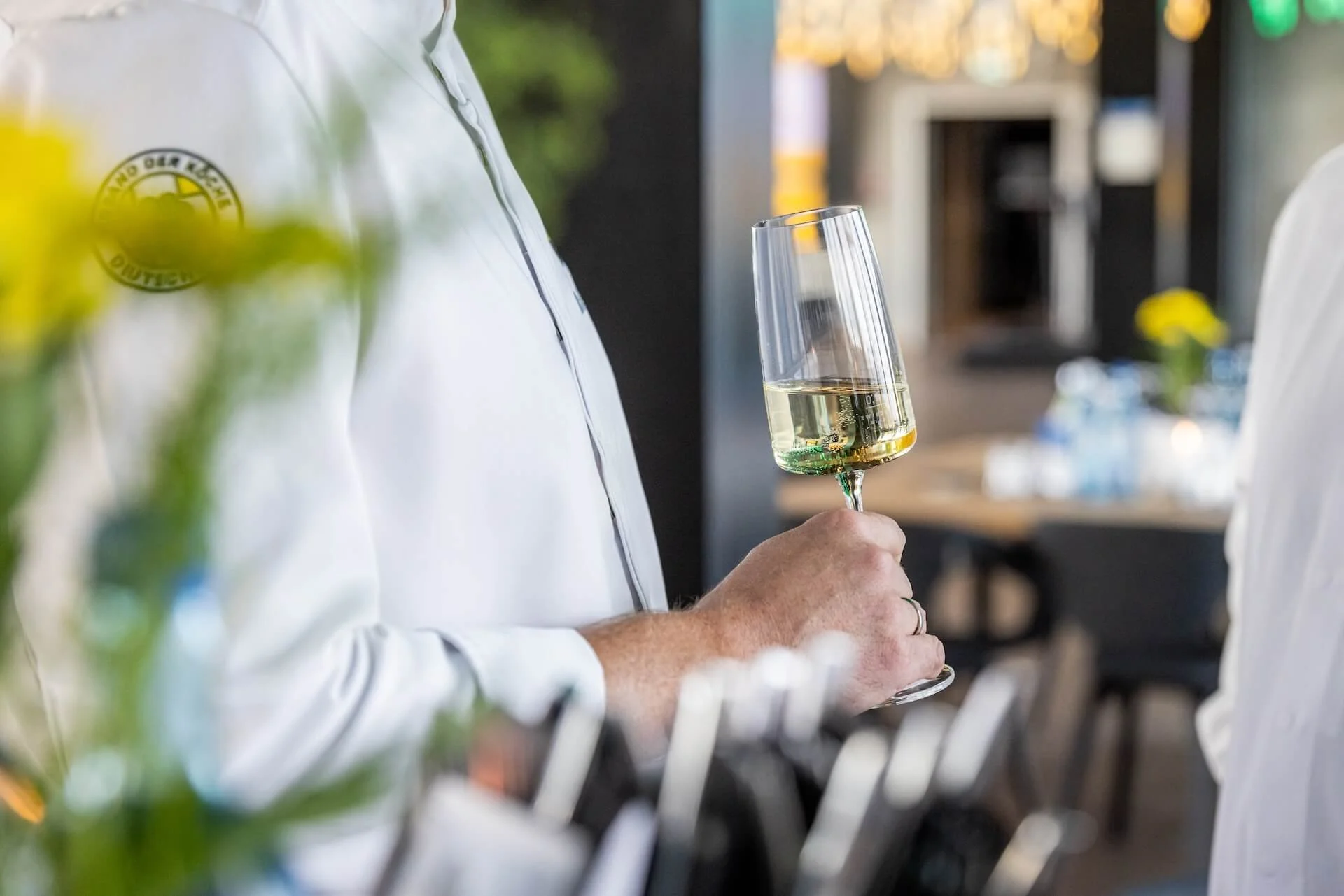 Person holding a glass of white wine at an outdoor event or restaurant.