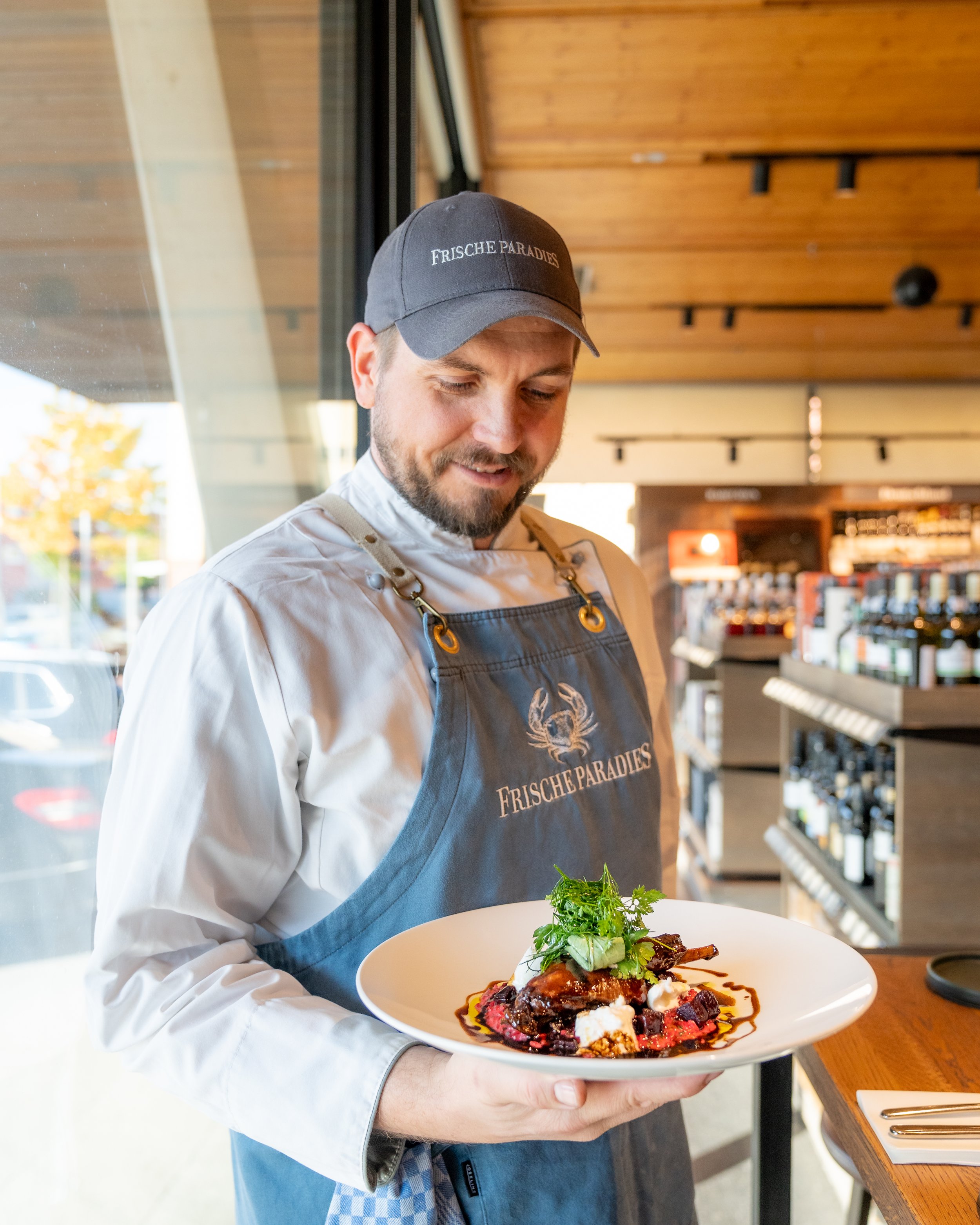 Chef holding a plate of gourmet food in a restaurant or cafe setting.