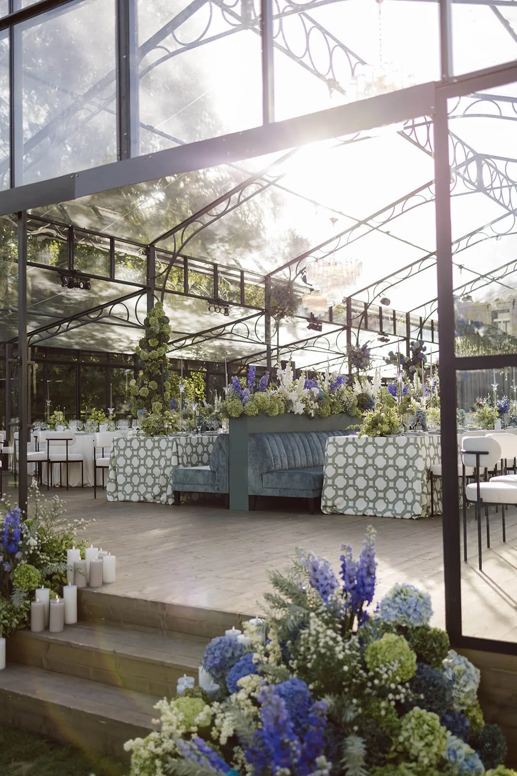 Elegant outdoor event space with floral arrangements, candles, and decorated tables, basking in bright sunlight.