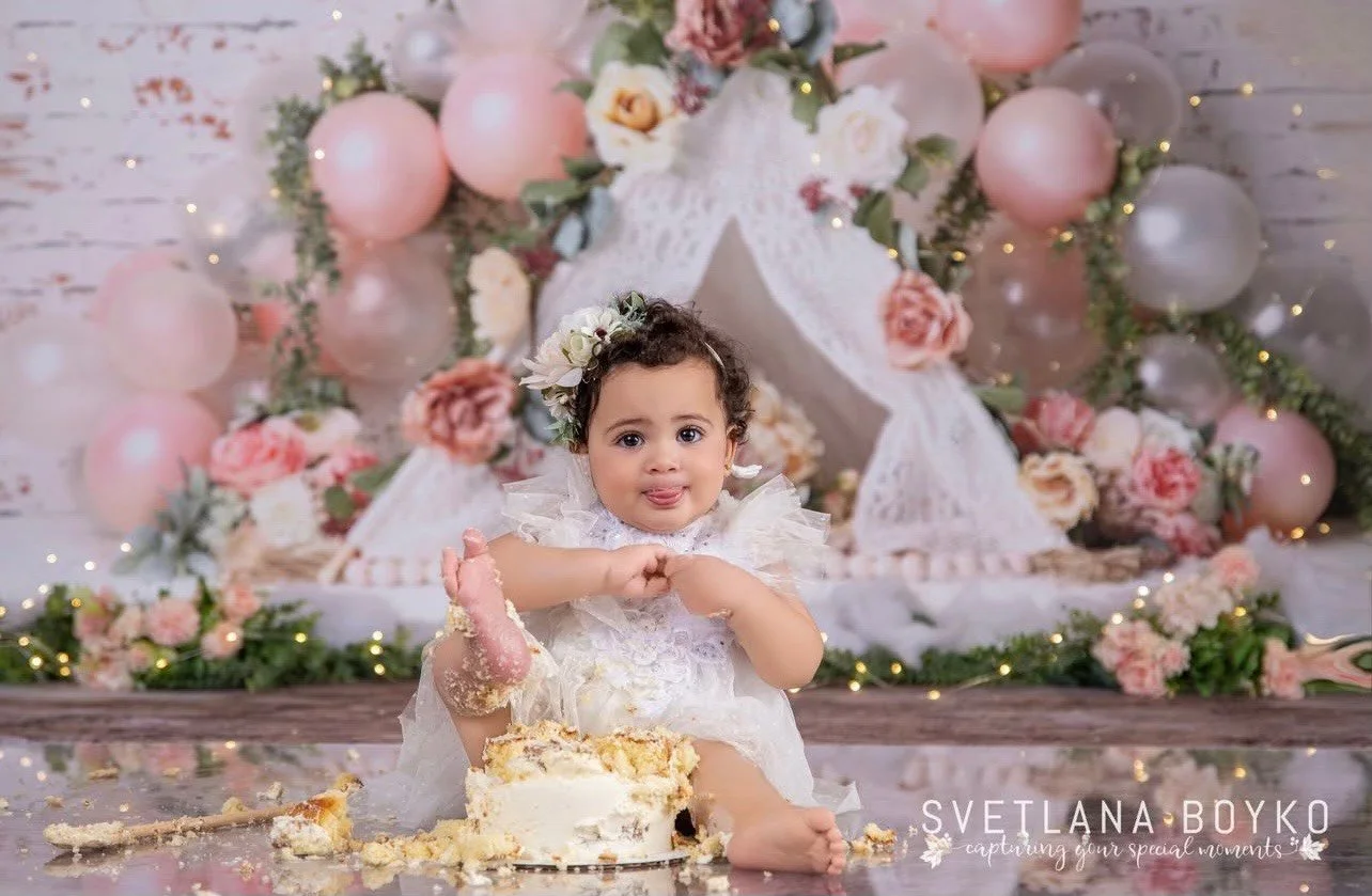 Baby girl celebrating her first birthday with a pink floral cake smash