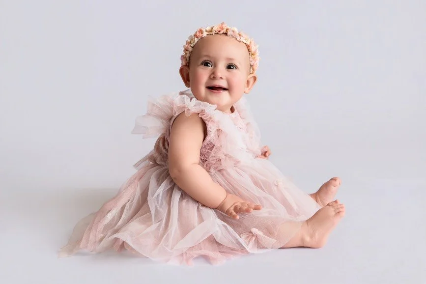 Smiling sitter baby girl photographed during a milestone session in a professional studio in Central New Jersey