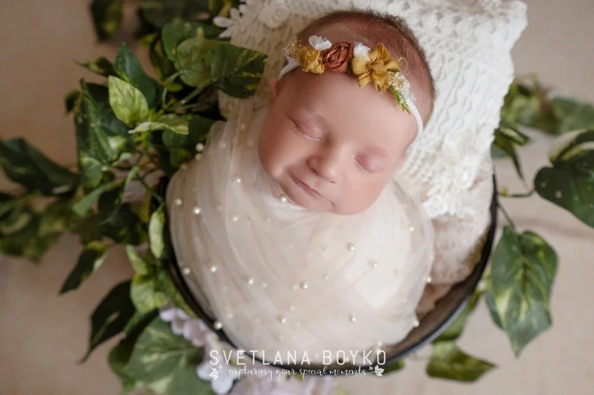 Sleeping newborn baby girl wrapped in a soft white wrap, photographed in a Central NJ studio.