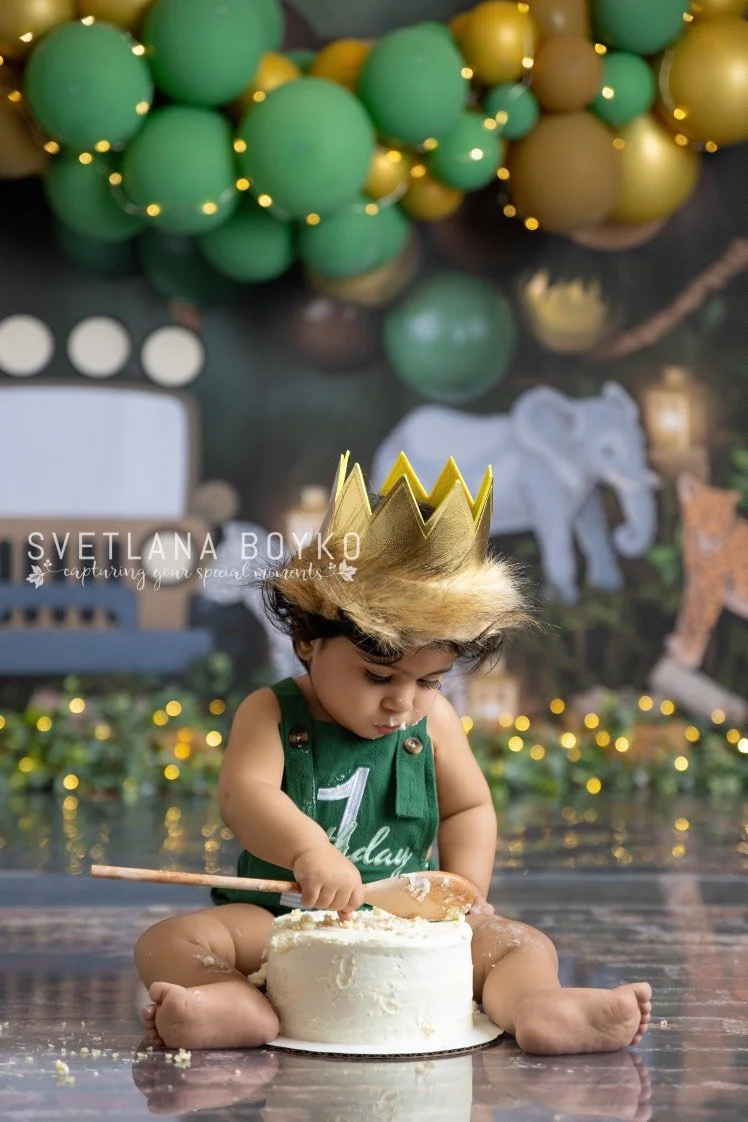 Baby boy wearing a crown during a green jungle first-birthday cake smash