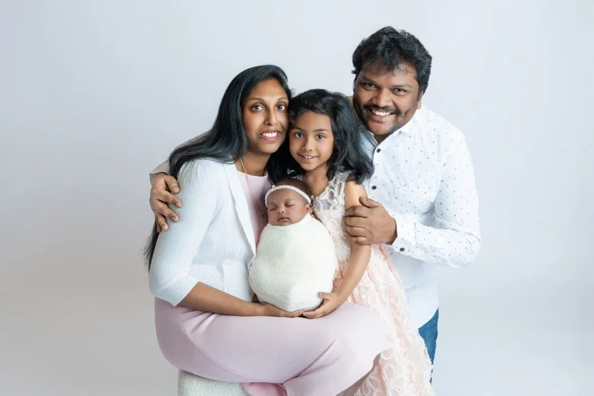 Family newborn portrait in studio featuring parents and older sister holding sleeping baby, professional newborn photography in Mercer County NJ and Bucks County PA