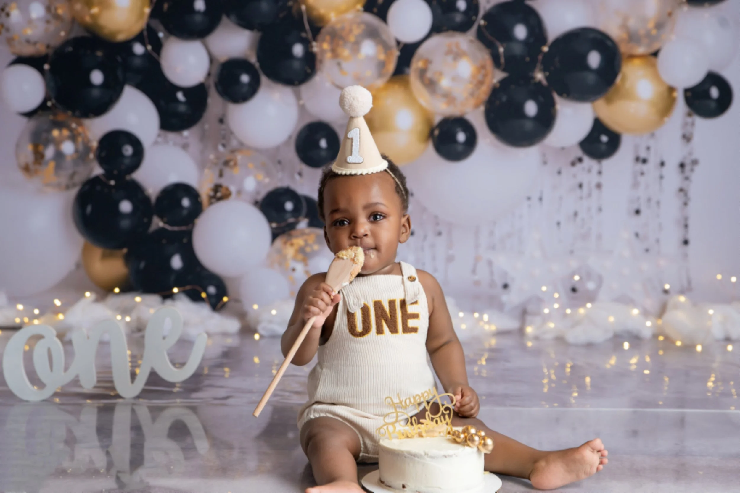 Baby celebrating a first birthday with a black, gold, and white cake smash setup
