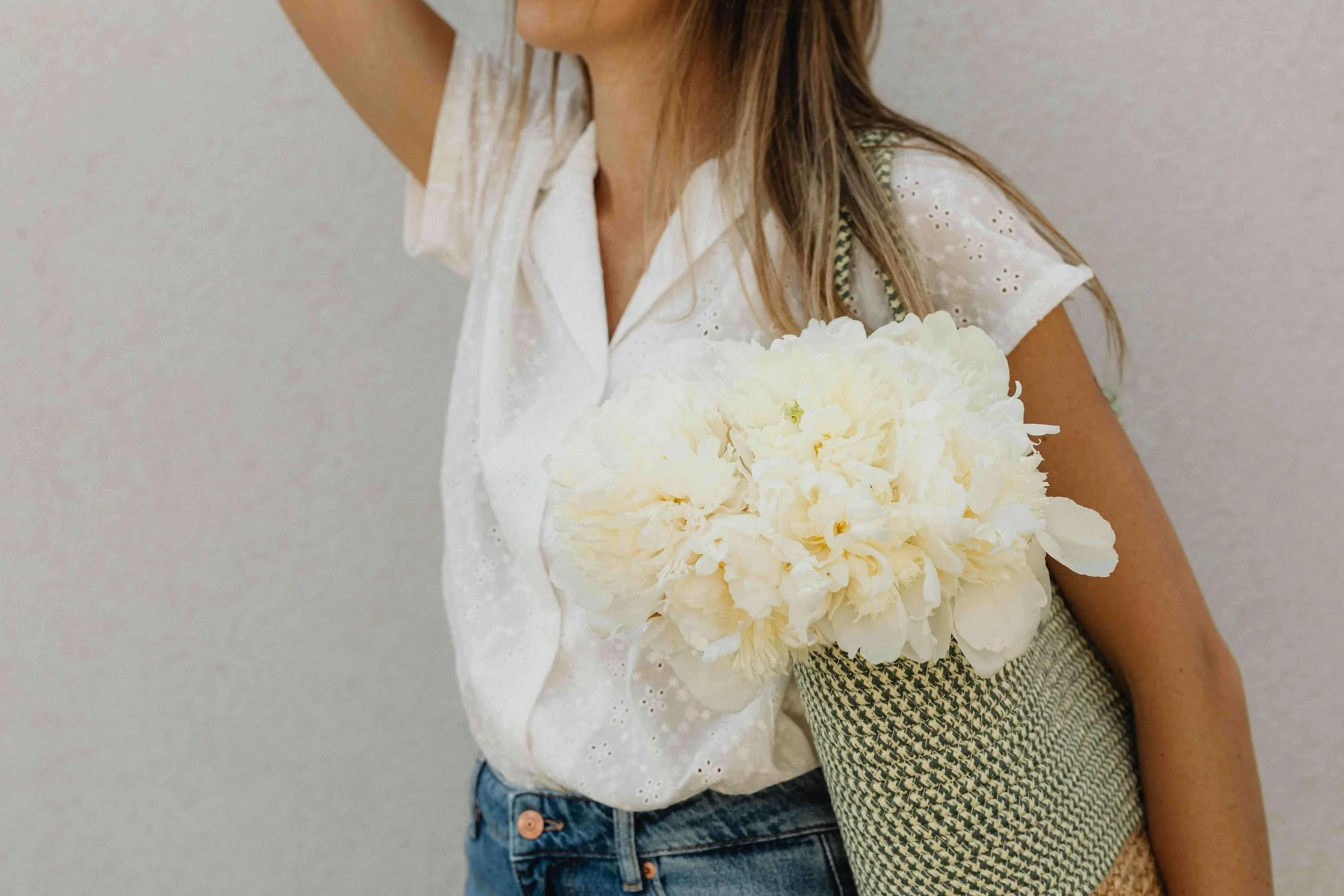 A woman holding a bouquet of white flowers against a neutral background.