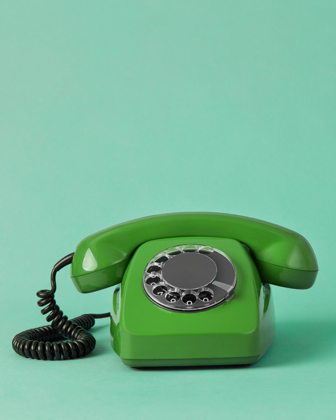 Green vintage rotary dial telephone on mint green background.