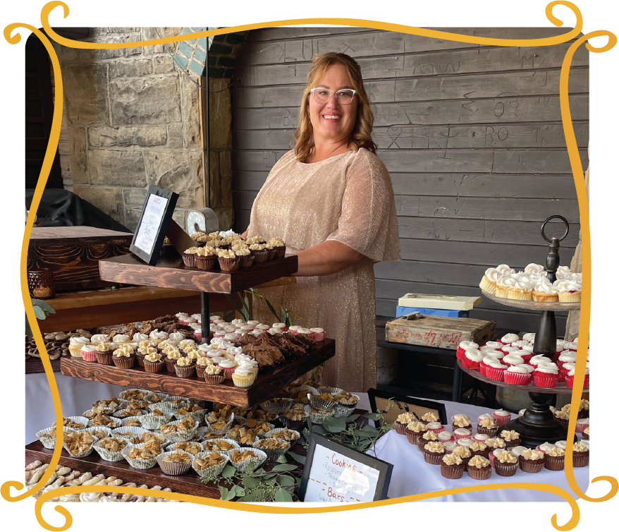 Kristine Clyde standing behind a display of homemade sweet treats, custom cookies, and pastries at Kristine’s Kitchen in Gillette, WY.