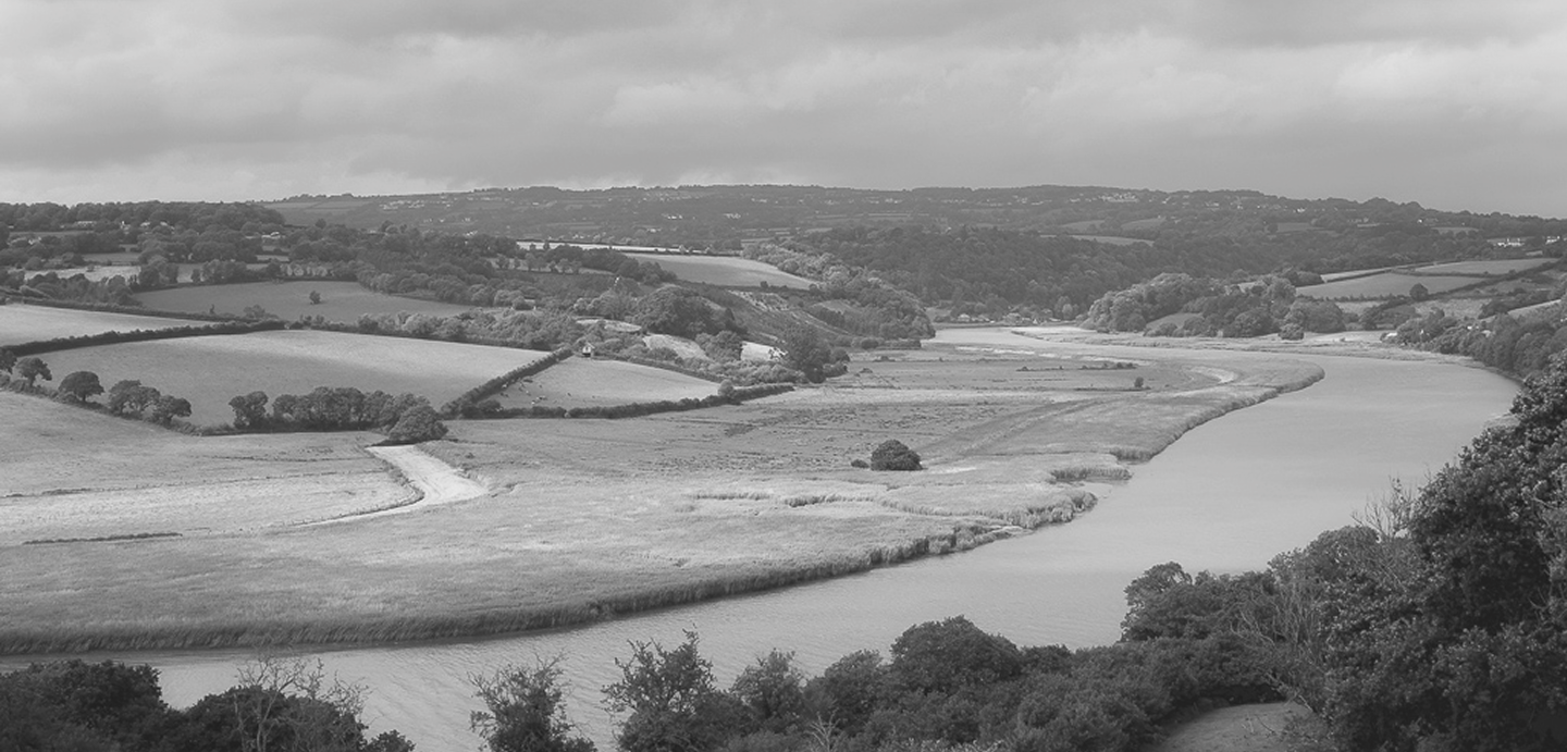 A black-and-white landscape of a river winding through rolling hills, with trees scattered across the fields and a cloudy sky overhead.