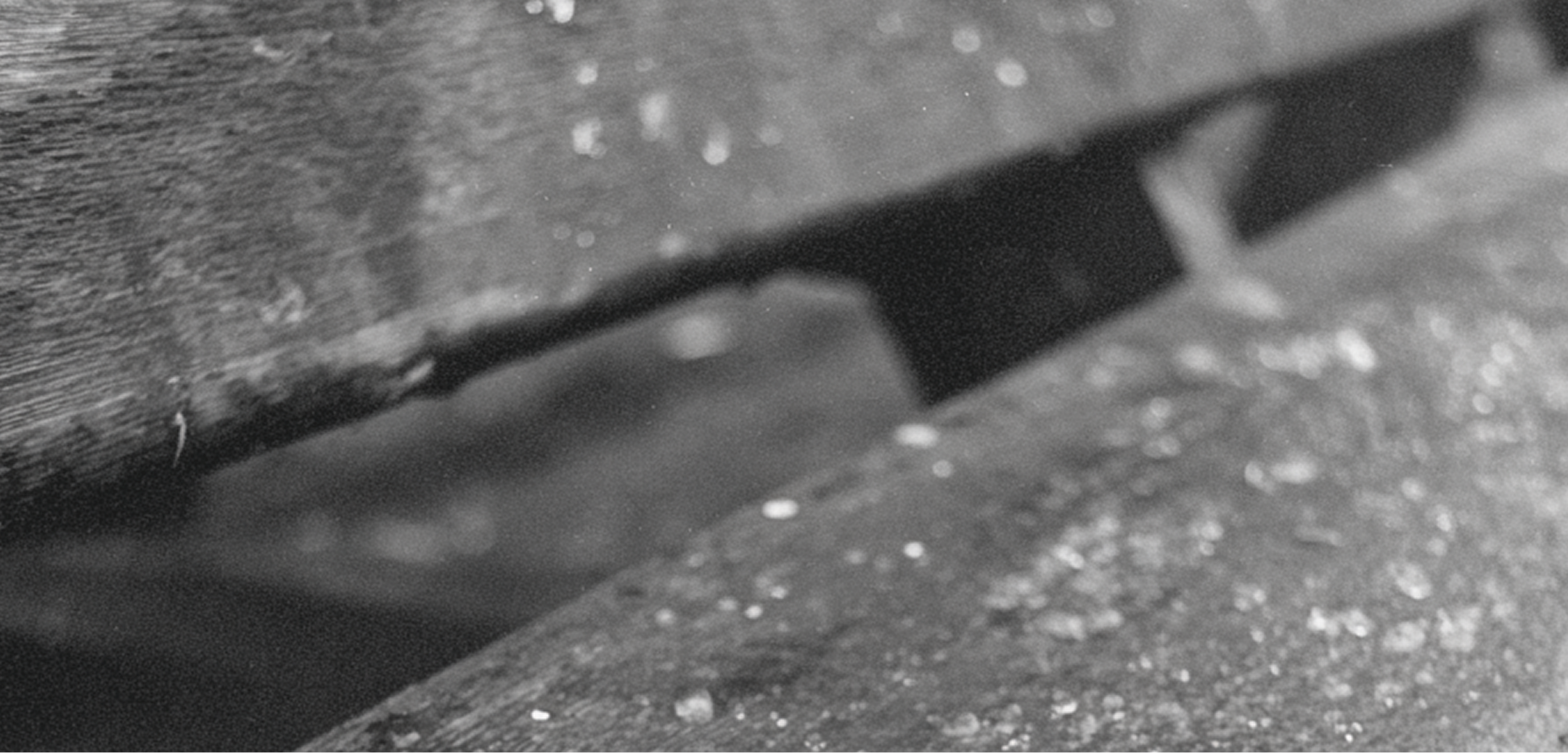 Close-up of a metal latch or hinge on a wooden surface, black and white photograph.