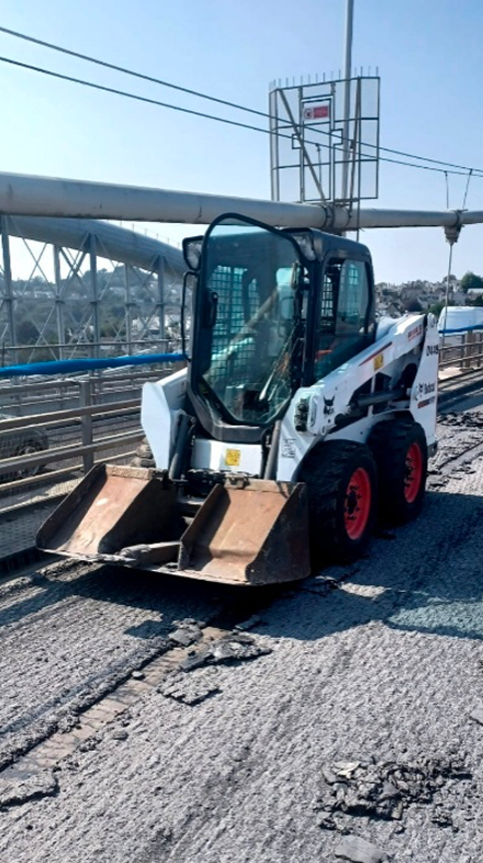 Small skid-steer loader on a bridge, working on asphalt resurfacing.