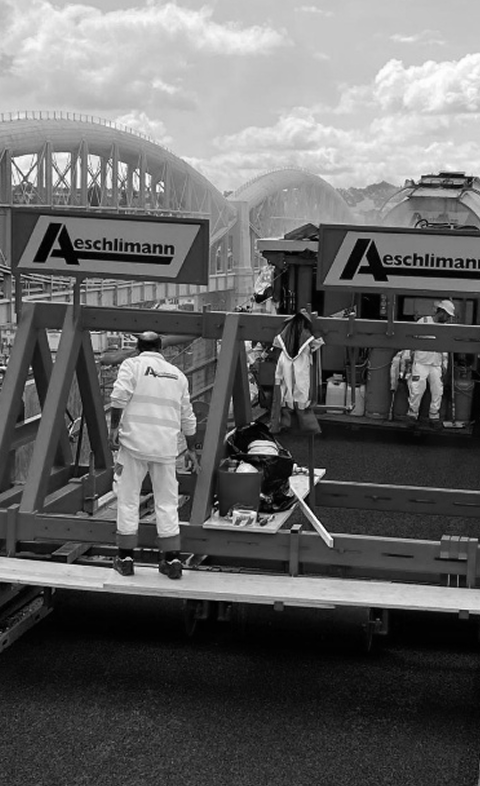Construction workers on a building site with cranes and large arched structures in the background, branding for Aschlimann.