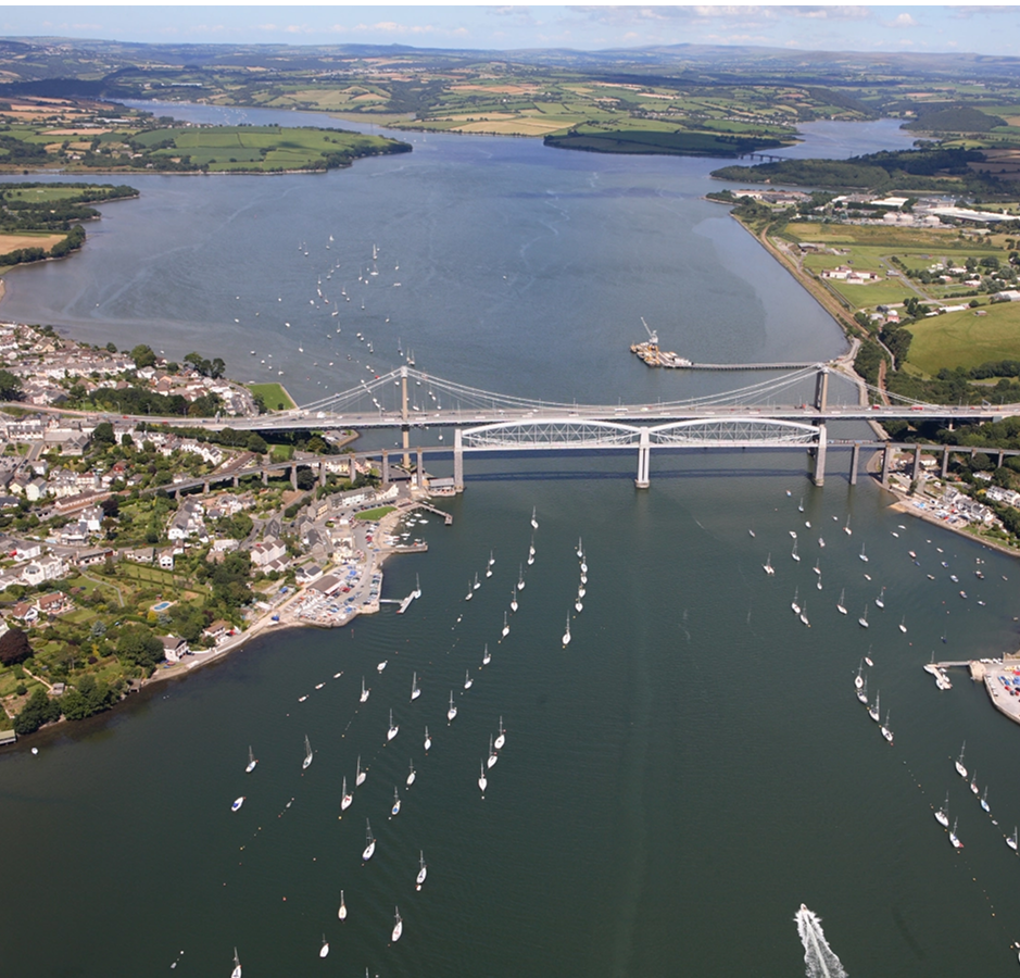 An aerial view of a bridge crossing a large body of water with many sailboats and a small town on the shoreline.