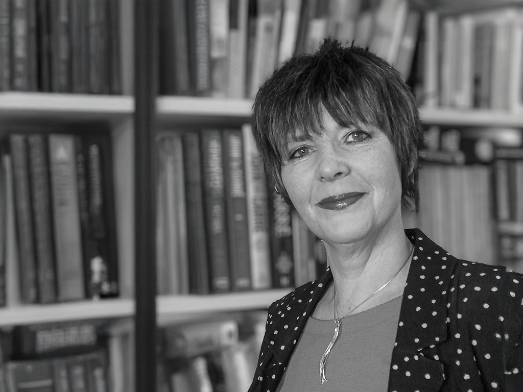 Trisha Hewitt smiling in front of a bookshelf filled with books.
