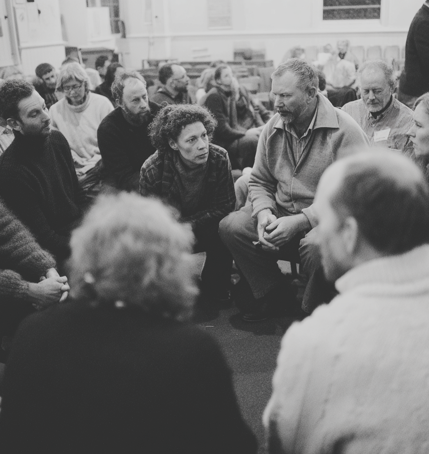 Group of people sitting on the floor engaged in a discussion, with one woman speaking and others listening attentively.