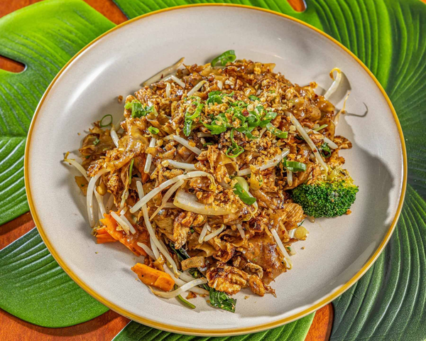Plate of stir-fried noodles with vegetables, topped with chopped green onions, served on a white dish with a yellow rim, on a green leaf-patterned placemat. Kaia's Kitchen Harristown