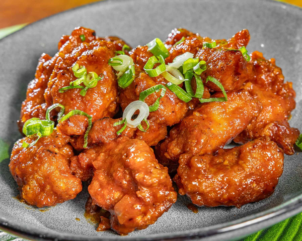 Fried chicken pieces coated in sauce, garnished with chopped green onions, on a gray plate. Kaia's Kitchen Harristown