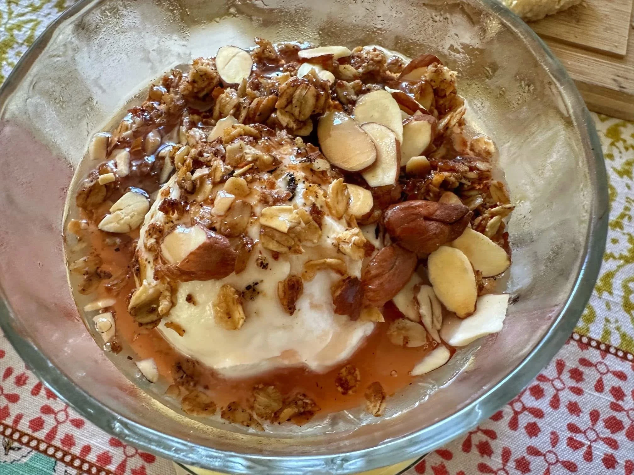 A glass bowl containing vanilla ice cream topped with chopped nuts, sliced almonds, pecans, and drizzled with caramel sauce.