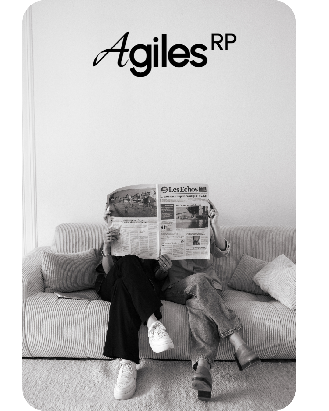 Une personne assise sur un canapé, portant des chaussures blanches, lisant un journal "Les Echos".