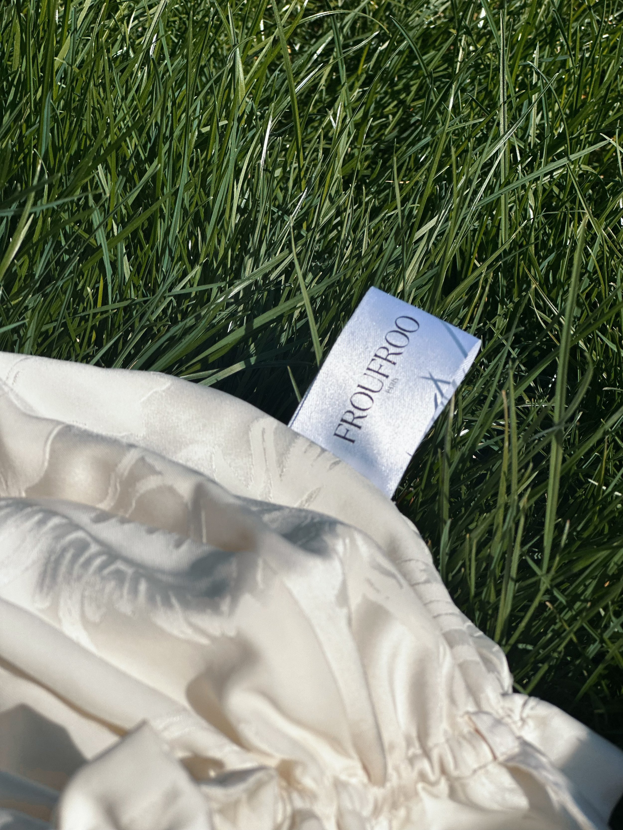 Un tissu blanc avec une étiquette indiquant 'FROUFROO' posé dans de l'herbe verte
