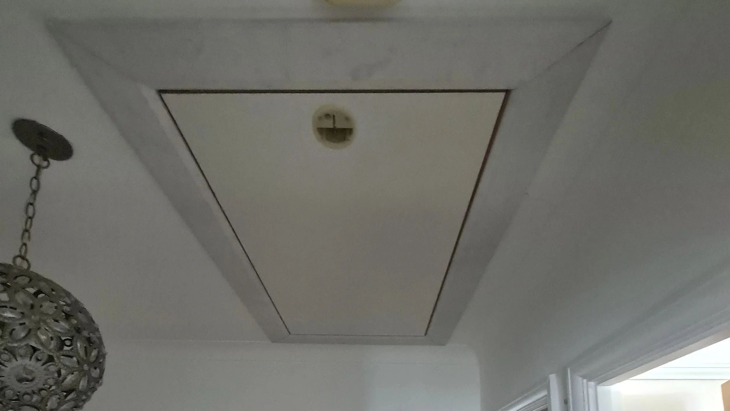 Ceiling access panel with a smoke detector and a hanging chandelier nearby in a room.