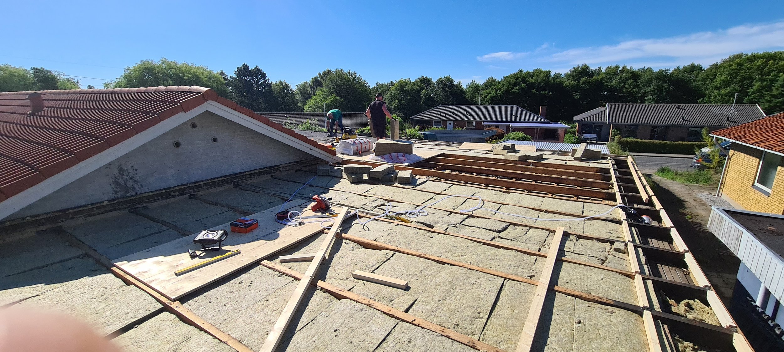 Workers installing new roofing on a house under clear blue skies, with construction tools and materials visible on the roof.