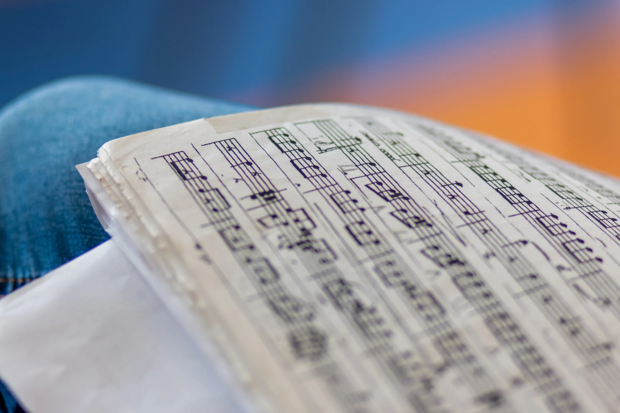 Partitura musical en papel en una persona que está sentada, con fondo borroso con tonos anaranjados y azules.
