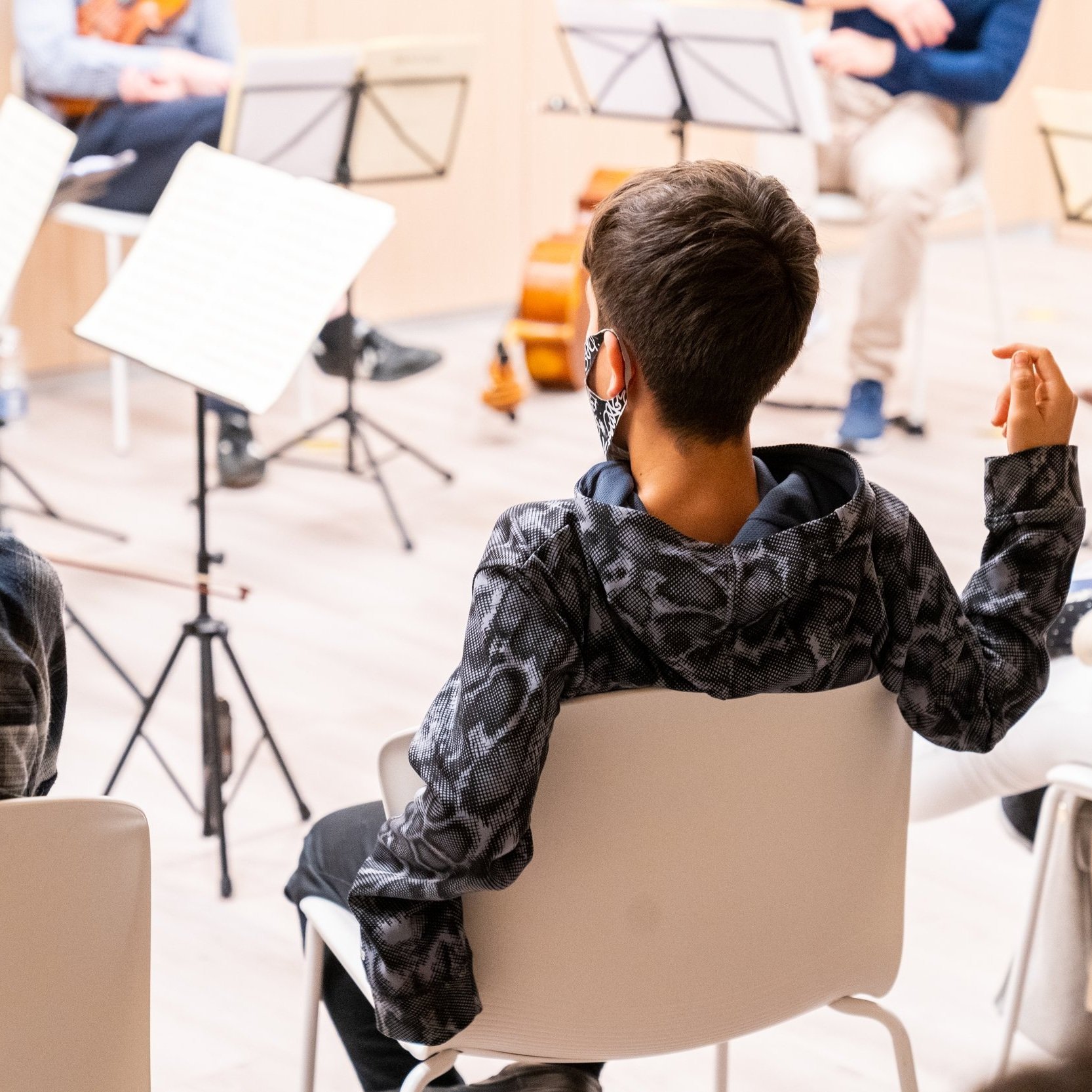 Persona joven sentada en una sala, con grupos de música y partituras, asistiendo a una clase o práctica de música.