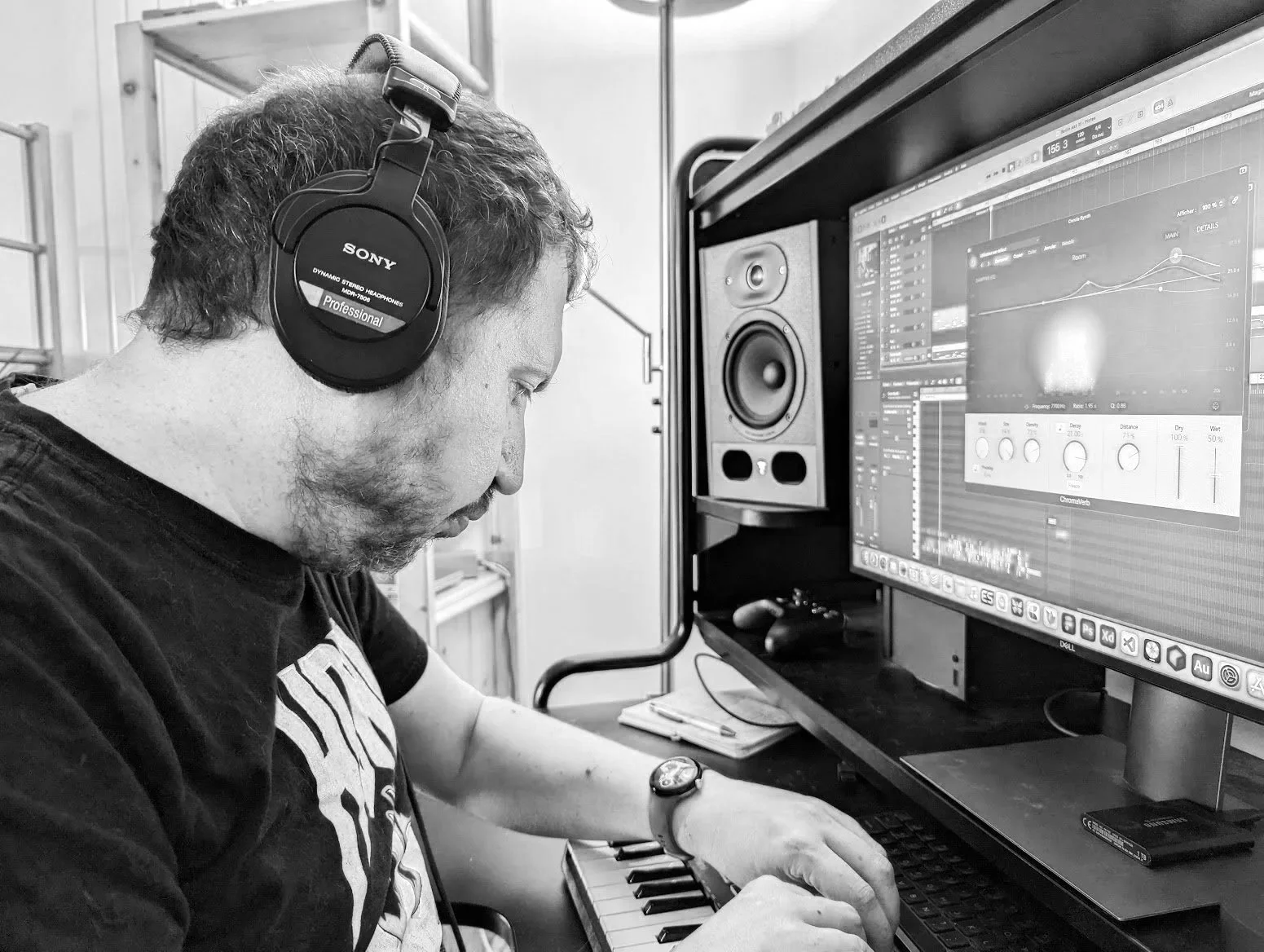 Un homme portant un casque d'écoute travaille sur un clavier de piano électronique avec un ordinateur affichant un logiciel de production musicale.