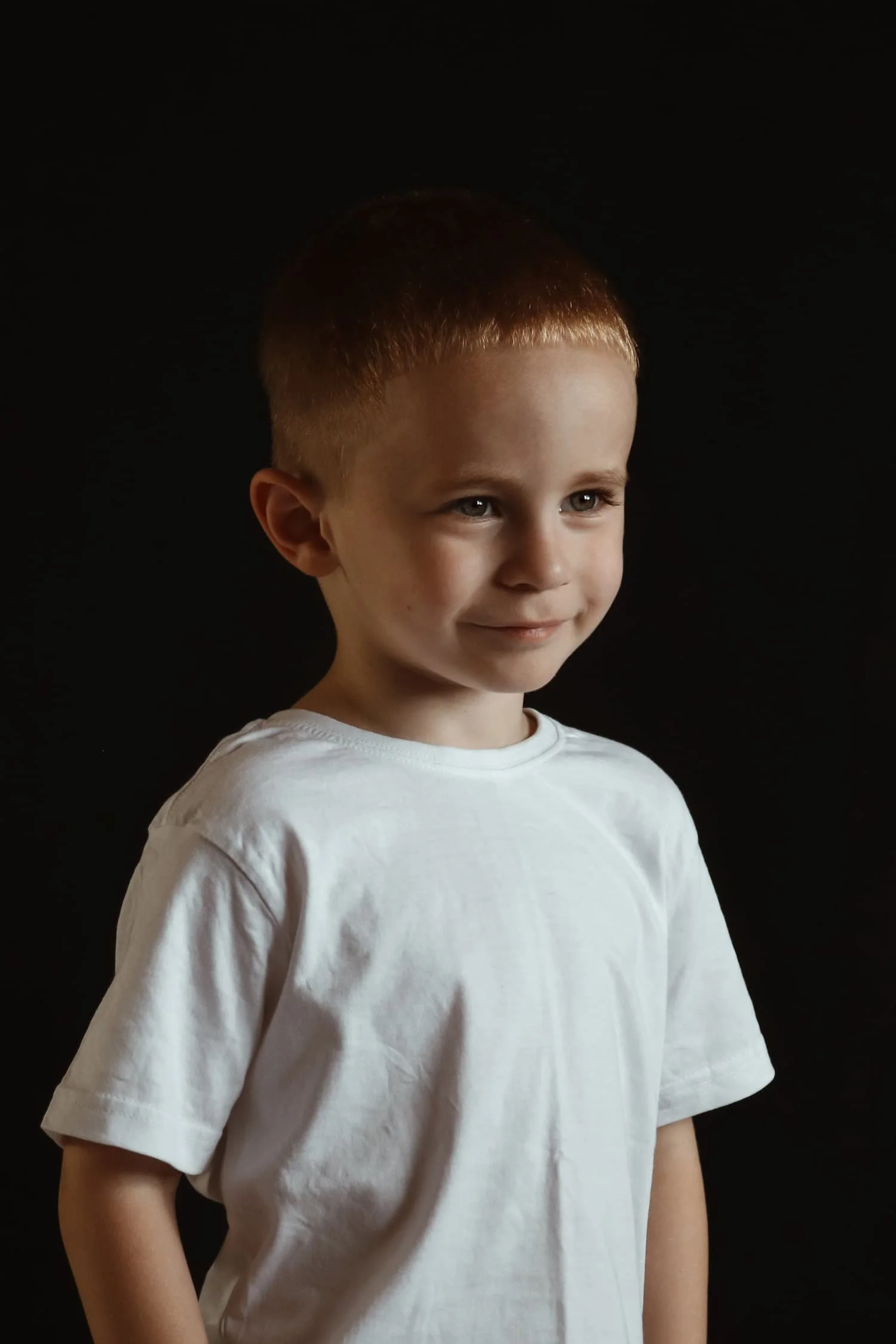 Fineart-Kinderporträt eines Jungen im weißen T-Shirt vor dunklem Hintergrund im Studio in Memmingen.