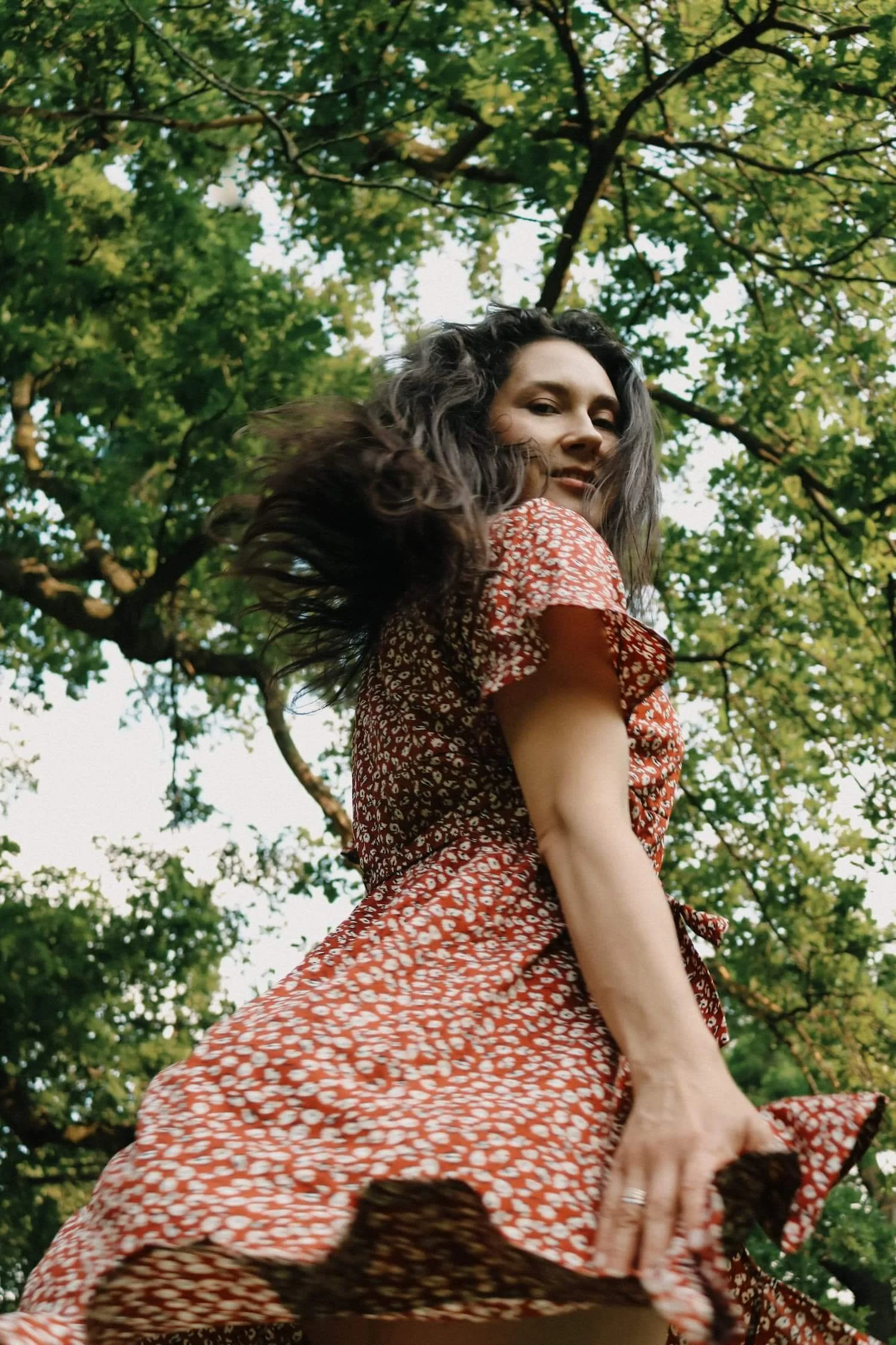 Lebendiges Fineart-Portrait einer Frau im roten Kleid, die sich drehend in der Natur bewegt, fotografiert in Ochsenhausen.
