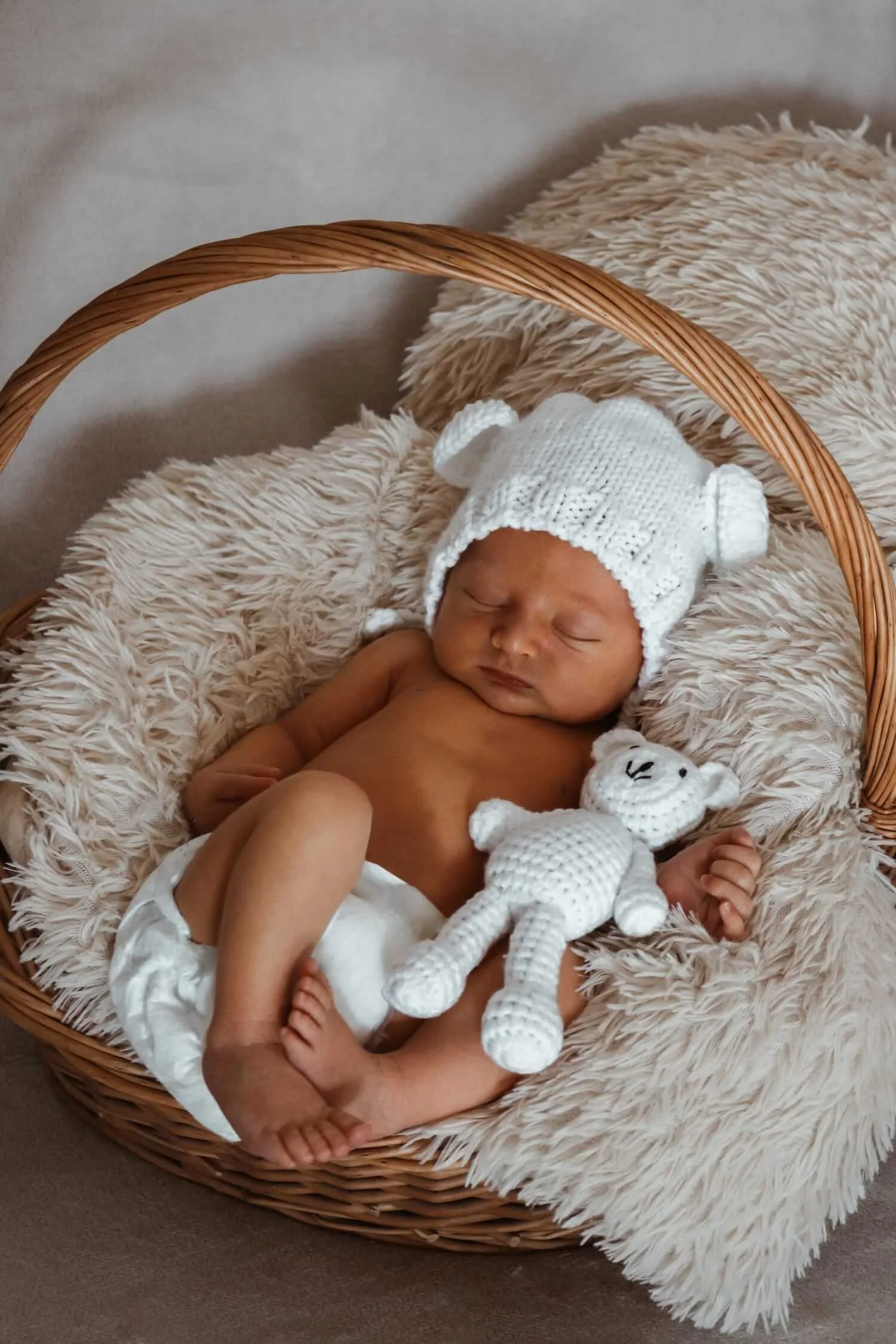 Schlafendes Neugeborenes mit Strickmütze liegt in einem Korb mit Kuscheltier, liebevolles Babyshooting im Fotostudio Ochsenhausen – OLONI Fotografie.