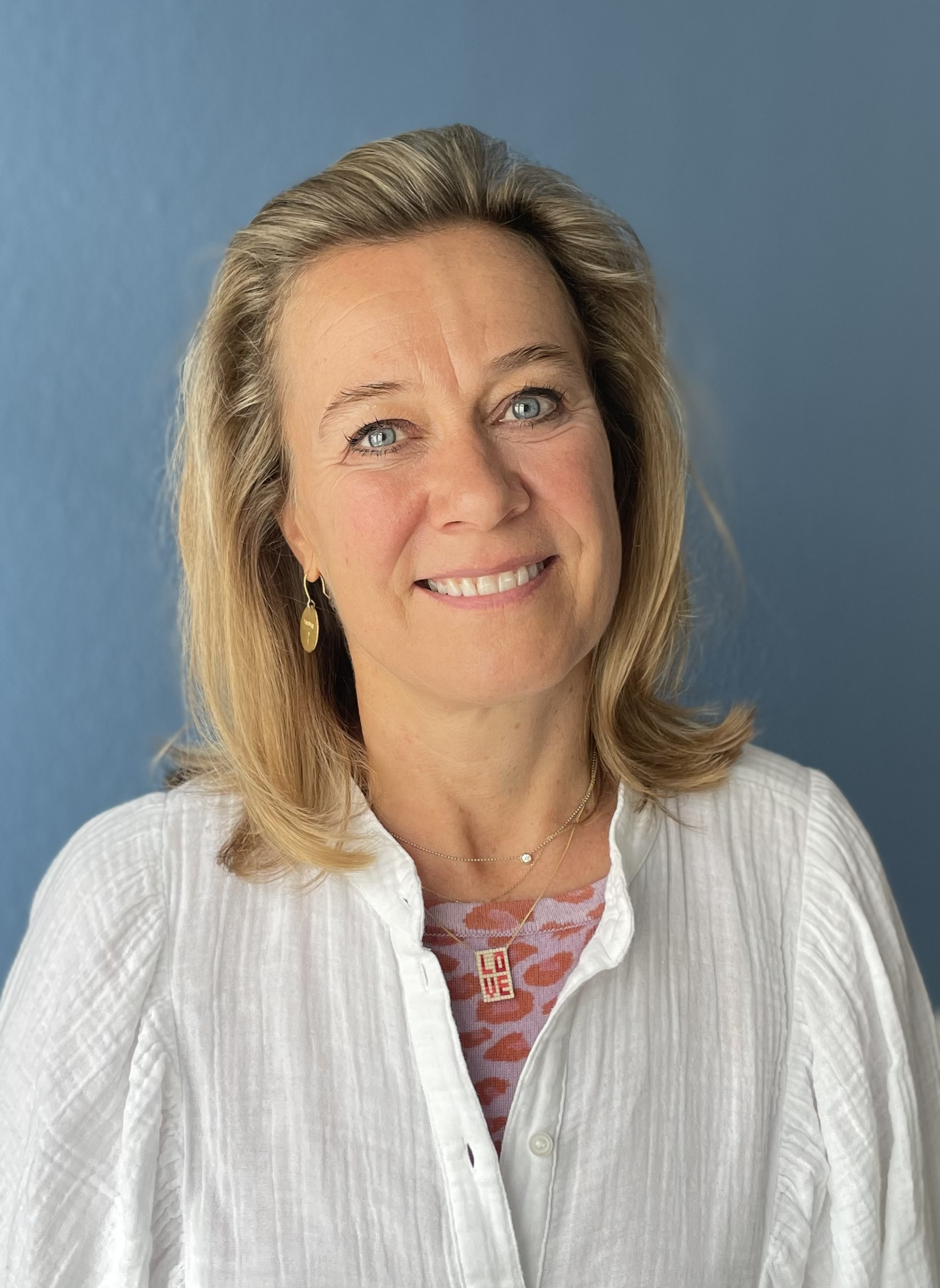 Porträt einer lachenden Frau mit blonden Haaren vor einem blauen Hintergrund.