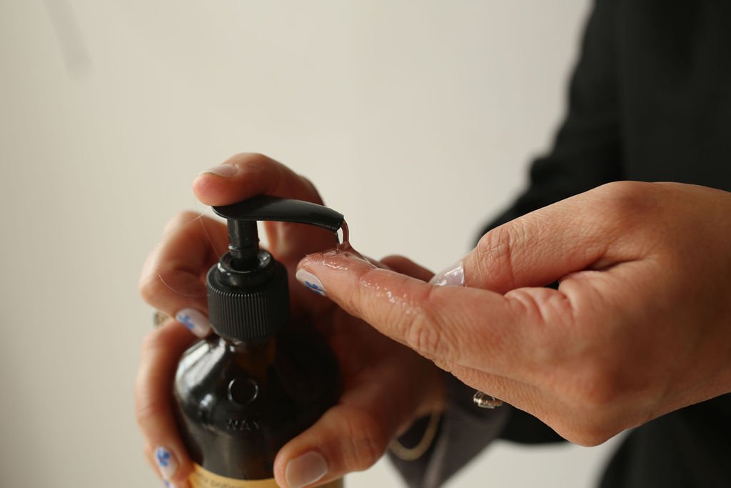 Person pressing a pump dispenser for hand sanitizer with one finger.