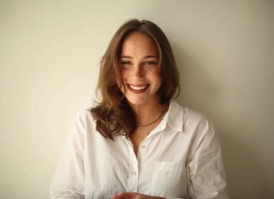 A young woman with brown hair in a white button down shirt is smiling 