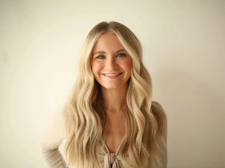 A young woman with blonde hair is smiling with a hand on her hip