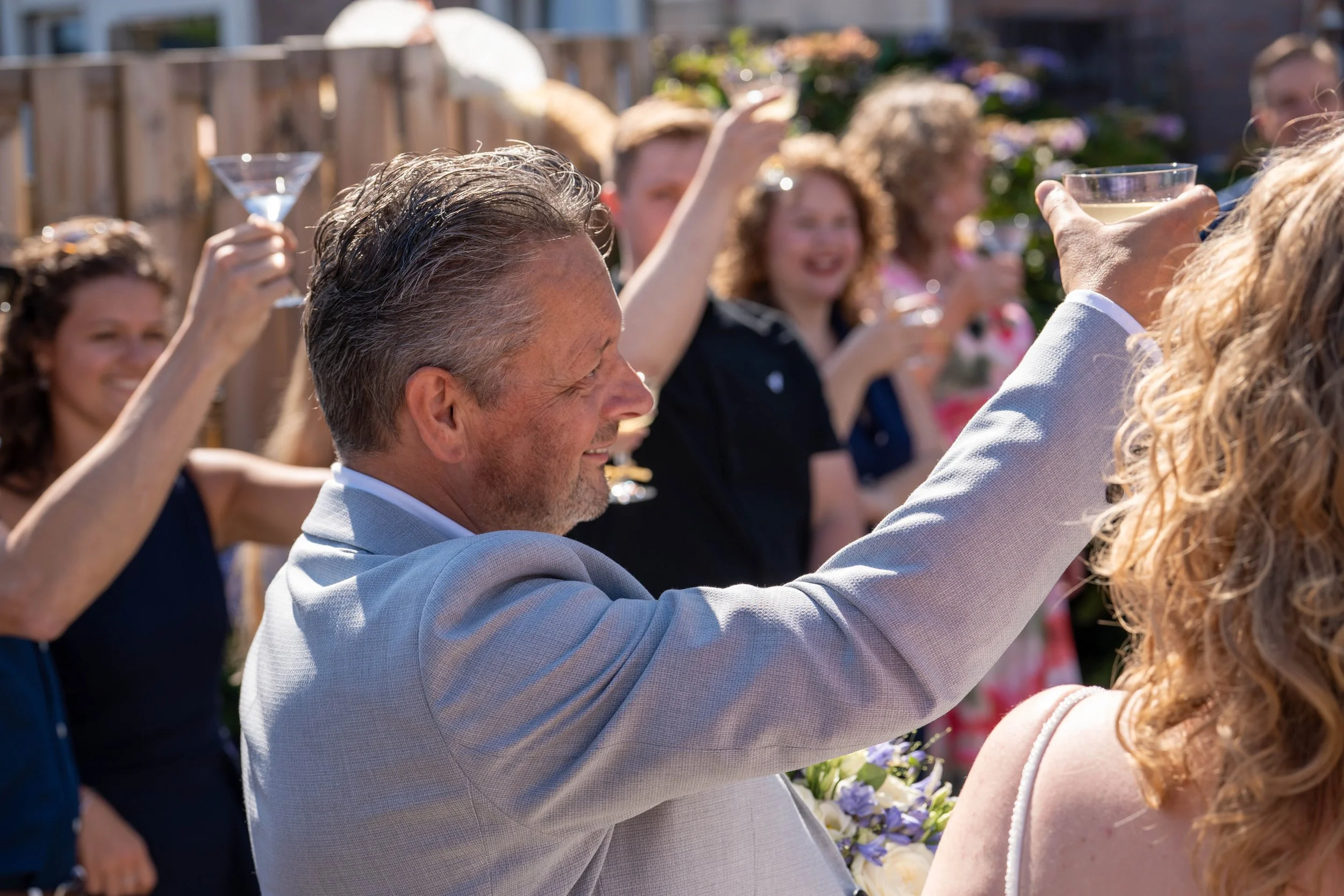 Bruiloftsfotografie van gasten die proosten tijdens een feestelijk moment buiten.