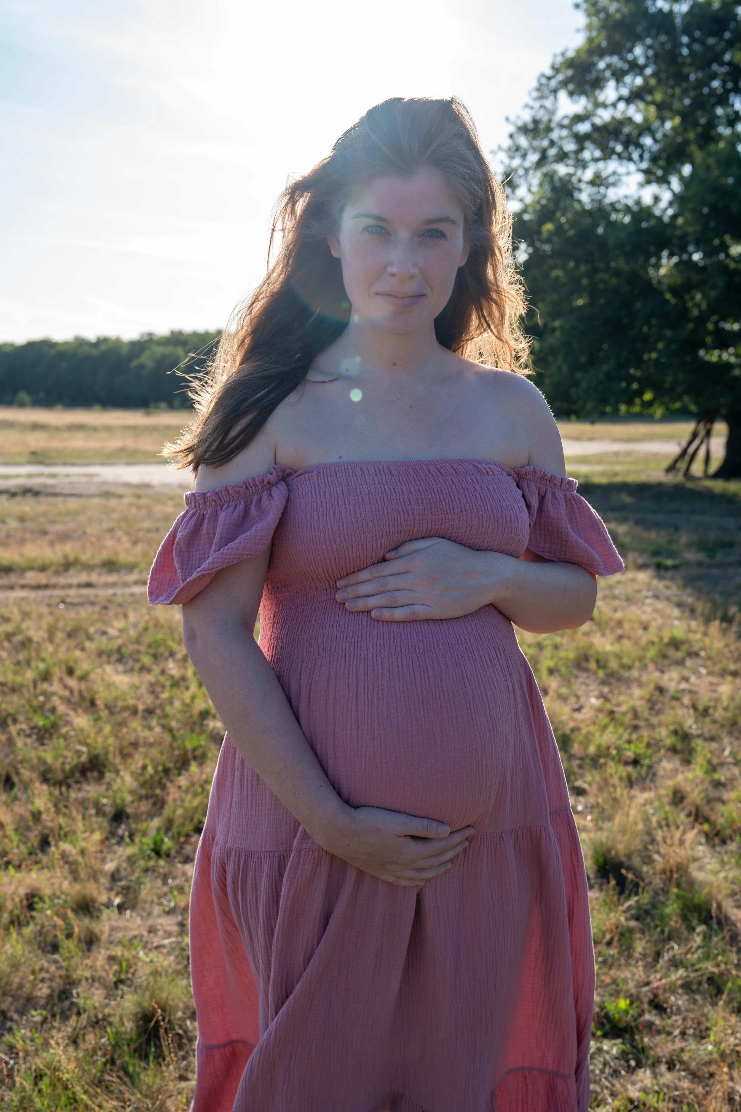 Zwangerschapsfotografie van een vrouw in roze jurk tijdens een natuurlijke buitenshoot.