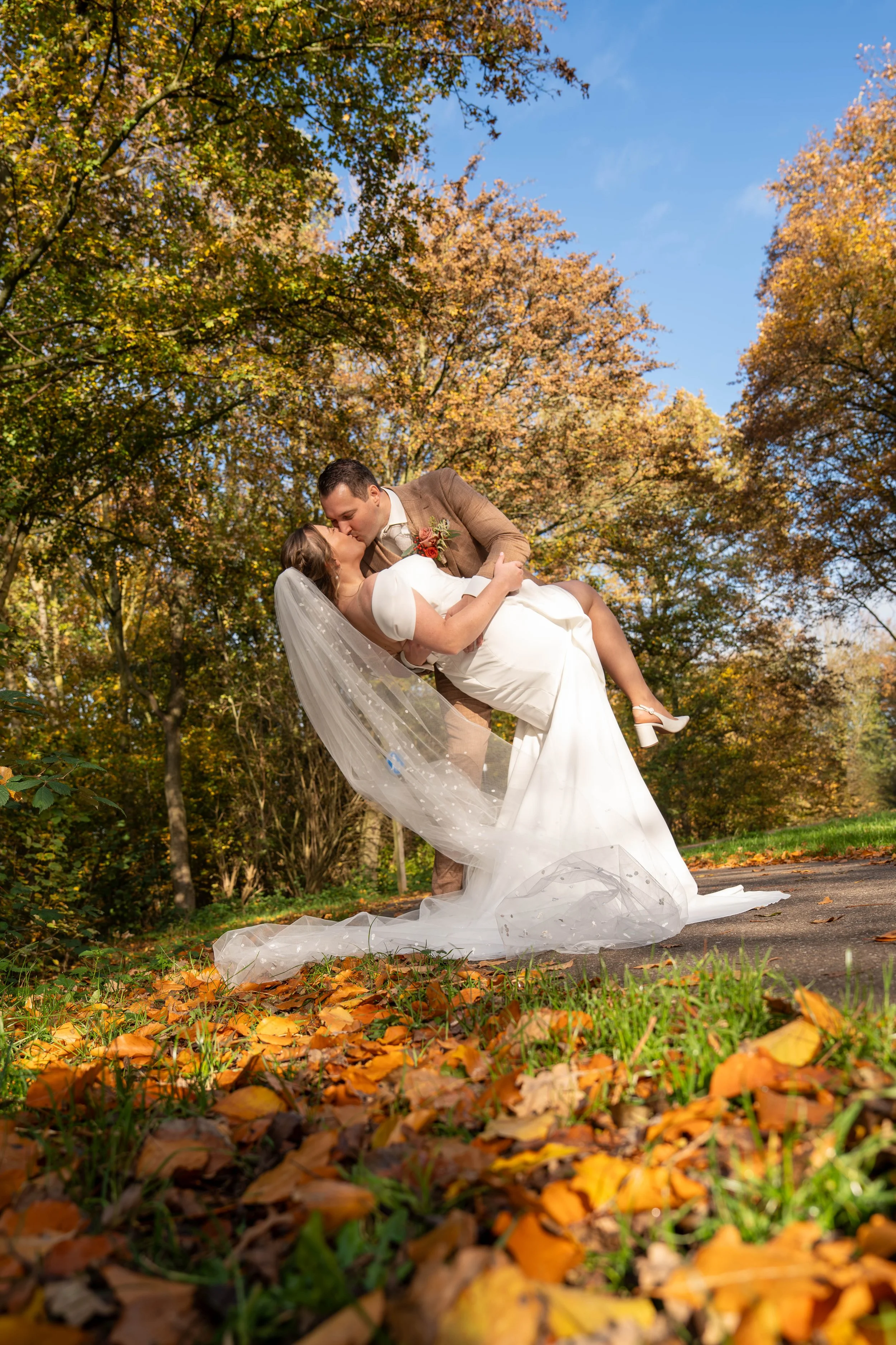 Trouwfotografie van een bruidspaar tijdens een romantisch moment in een herfstachtige buitenomgeving.