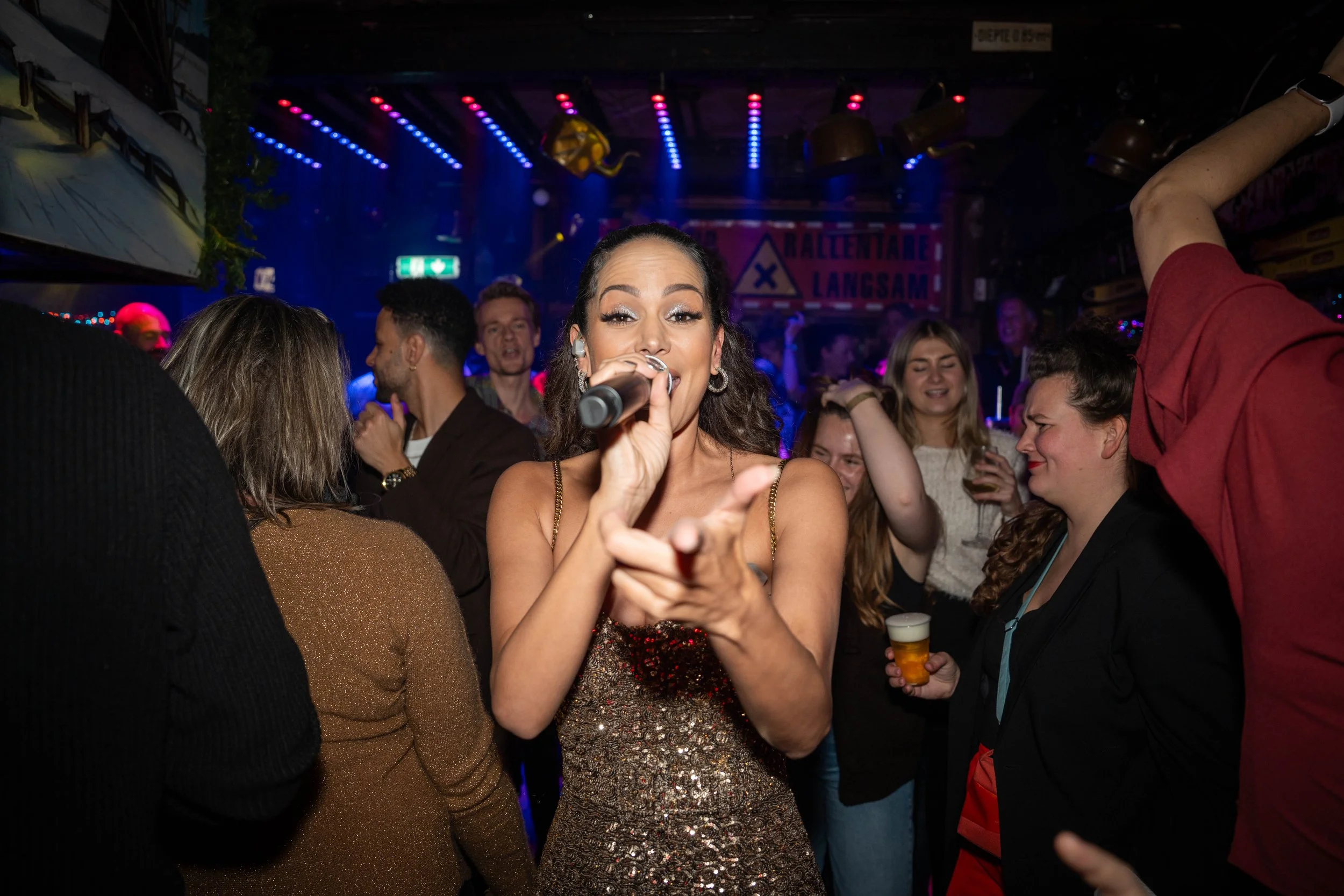 Eventfotografie van een zangeres met microfoon tijdens een feestelijk optreden met publiek.